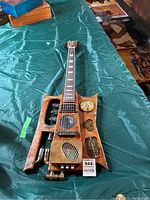 Full view of the faux guitar lying on a green cloth, showing the whole body and neck with its unique steampunk features.