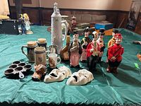 Full lot display showing all decanters, steins, theatre masks, bottles, and cast iron mould on table