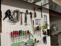 Full view of tools arranged on pegboard in basement workshop including clamps, screwdrivers, hammer, wrenches, and other hand tools