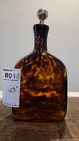 Front view of tortoise shell Venetian glass decanter with metal stopper and cork wrap. Marked 12.5 inches tall.