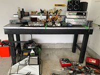 Full view of the large wooden work bench with metal top, showing its height and length, along with various items on and below it that are not included in the sale.