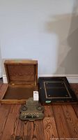 Two wooden writing boxes and one brass pen holder displayed on wooden floor. One box opened showing interior surface; the other with decorated black top. Brass pen holder is ornate with intricate pattern.