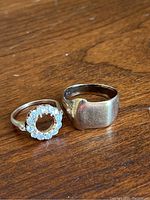 Two rings side by side on wooden surface, showing signet ring and circle stone ring overview