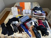 Overview of women's accessories on bed including scarves, gloves, clothing, and shopping bags from designers