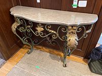 Front angled view showing green wrought iron scroll legs with gold leaf accents and beige marble top with detailed edge.