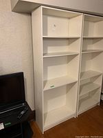 Front view of two white laminated plywood bookcases with three shelves each.