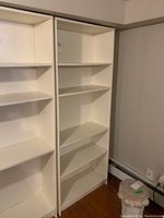 Front view of two white laminated plywood bookcases with four shelves each, placed side by side in a room.