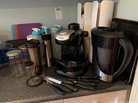 Photo showing coffee maker, knives, cutting boards, beverage containers and jars on counter.