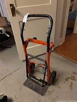 Front view of metal dolly showing handle, base plate, and wheel configuration.