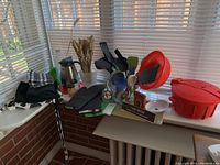Full view of kitchenware lot on windowsill, including salad spinner, utensils, mitts, coffee pot, cloths, tin, timer, and toothpicks.