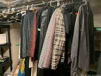 Varied women's coats hanging on rod in basement, showing different colors and patterns including black, red, and checkered design