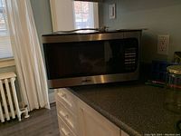 Microwave placed on kitchen counter with visible cord and part of instruction manual on top.