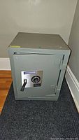 Front view of gray Sears safe box closed, showing handle, combination dial, and brand logo.