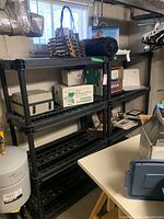 Image of one black plastic shelving unit with boxes and items on shelves, located in basement area.