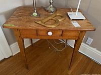 Front view of rustic wooden side table showing single drawer with ceramic knob and tapered legs on wooden floor.