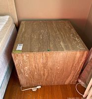 Front view of square stone side table placed next to a mattress.