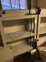 Two grey plastic utility shelves, each with four shelves assembled, placed against basement wall beneath a window. Shelves appear clean and structurally sound.