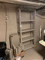 Assembled plastic utility shelving unit with five shelves against a basement wall, showing the full height and number of shelves.