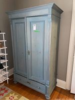 Front view of blue wooden wardrobe with closed two-panel doors and bottom drawer.