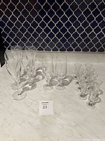 Full shot showing 4 champagne flutes, 2 tall glasses, 10 shot glasses arranged on marble surface