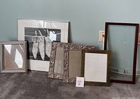 Wide shot showing six assorted size frames, mostly metal with one wood frame and a framed black and white print.