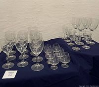 Photo shows three groups of clear glassware on a blue cloth, including 6 brandy snifters, 6 wine glasses, and 7 smaller glasses.