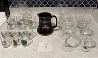 Wide view of nine various German wine glasses and one black Glenfiddich water jug arranged on countertop.