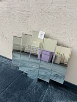 Five-panel Mid Century Modern wall mirror leaning against a textured wall on blue carpet.