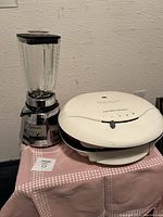 Photo showing Hamilton Beach sandwich press and Osterizer blender on a table with a pink patterned cloth.