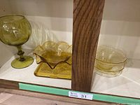 Shelf display with green Viking amber compote goblet on the left, a yellow scalloped bowl front right, a yellow ribbed dish center back, and a smaller green bowl on the right