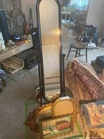 Large full-length standing mirror with black frame and base, along with three smaller gold framed mirrors leaning against couch and floor.