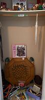 Photo of lower closet with wooden octagonal chess/checker board, assorted playing pieces, and a pink 500 piece puzzle box