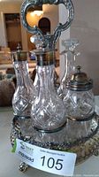 Front view of the cruet set showing four crystal glass bottles with silver plate tops arranged in an ornate silver plate base with decorative handle