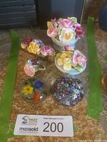 Full lot showing three floral bone china arrangements and three smaller glass and china decor pieces on carpeted floor with auction sign.