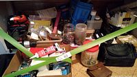 Boxes and containers of assorted nails, screws, adhesives, hand tools, and storage jars with hardware items inside in a packed cardboard box.