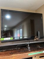 Front view of the Insignia 38 inch TV on a wooden stand with the remote control placed beside it and coiled power cord.