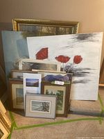 Group of assorted framed paintings and prints leaning against a wall, including a large abstract floral painting with red petals and several smaller framed nature prints.