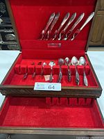 Photo of the entire cutlery set displayed in open wooden case with red velvet lining, showing knives at top lid and other utensils below.