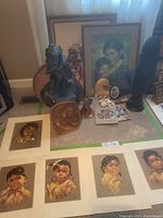 Display of assorted Indigenous art pieces including framed portraits, wooden carvings, and sculptures on beige carpet.