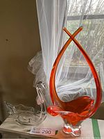 Photo showing both the bright orange swing glass vase and clear crystal swan bowl together by window light.