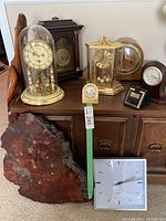 Photo of various table clocks on a wooden cabinet, showing a mix of materials including glass dome, brass, wood, and marble