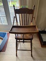 Front view of vintage wooden high chair showing carved backrest and attached tray.