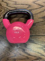 Photo shows one pink 15 lb kettlebell dumbbell with a black handle and AmazonBasics branding on the front, placed on a wooden surface.