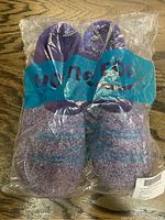 Photo of a new pair of purple HomeTop women's memory foam slip-on house slippers in clear plastic packaging with HomeTop branding.