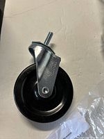 Close-up photo of a single caster wheel showing metal mounting bracket and black plastic wheel.