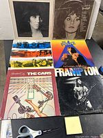 Photo displaying six vinyl album covers including Linda Ronstadt, The Police, The Cars, Heart, and Peter Frampton. Scissors visible on the table for scale.