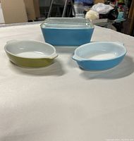Three vintage Pyrex mini casserole dishes displayed together; two oval dishes (blue and green) and one covered rectangular blue dish.