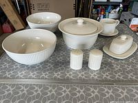 Photo showing entire set of white ceramic serving pieces on table: 2 large bowls, covered vegetable dish, salt and pepper shakers, butter dish, gravy boat with saucer.