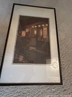 Full view of framed Asian print showing scene in warm tones with mat and frame on carpet.