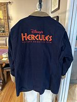 Back view showing the embroidered Disney's Hercules Feature Animation Crew logo in large orange and red text.